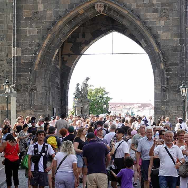 Multitud de turistas aglomerados bajo la torre del Puente de Carlos en Praga durante un día de verano.