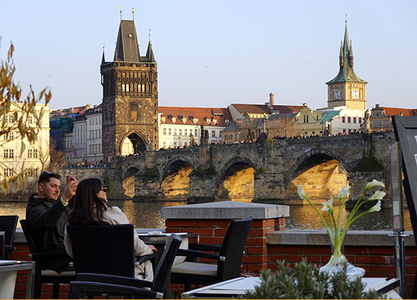 Pareja disfrutando de una cerveza con vistas al Puente de Carlos en el tour de Praga en un día.