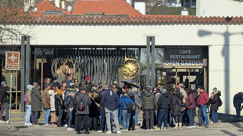 Grupo grande de unos 60 turistas rodeando a un guía con paraguas abierto en una plaza de Praga antes de comenzar un tour gratuito.