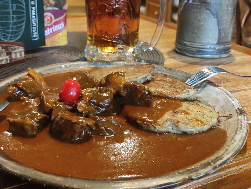 Plato auténtico de goulash checo de ternera servido con tortitas de patata (bramborák) y una jarra de cerveza local, comida tradicional en Praga.