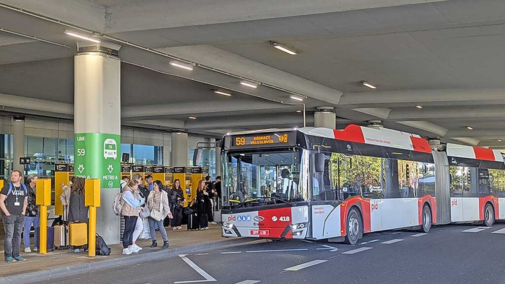 Nuevo trolebús 59 de Praga estacionado en la terminal del aeropuerto, junto a la columna informativa verde y máquinas de tickets amarillas.