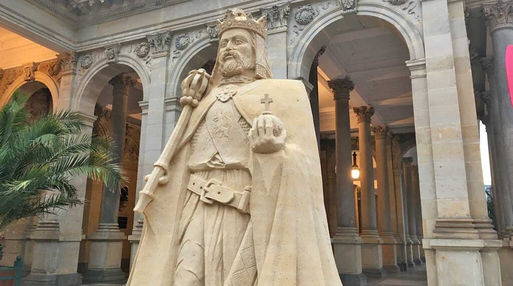 Escultura detallada en arena del rey Carlos IV frente a las columnas de piedra de estilo corintio de la Columnata del Molino en Karlovy Vary.