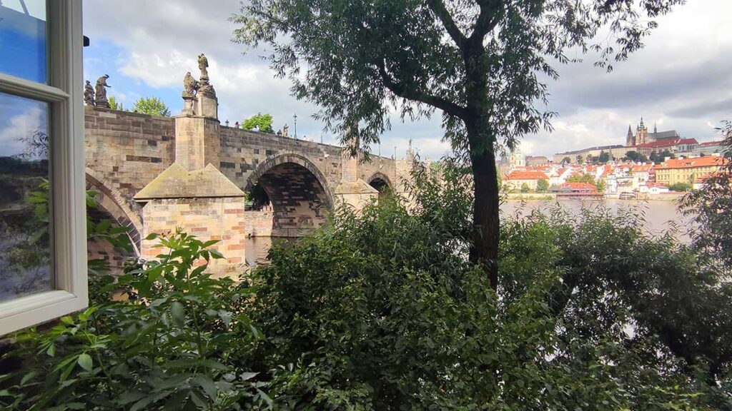 Vista panorámica del Puente de Carlos despejado a media mañana desde el Museo del Puente, con el río Moldava y la silueta del Castillo de Praga al fondo.