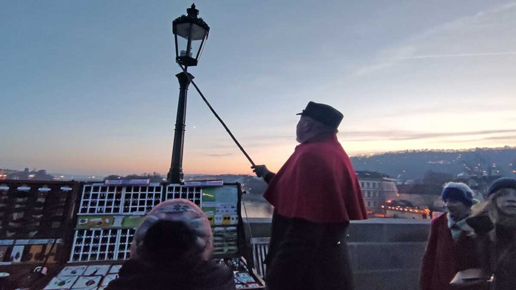Farolero de Praga en un día muy frío de Adviento encendiendo farolas frente a peatones abrigados con gorro y bufanda
