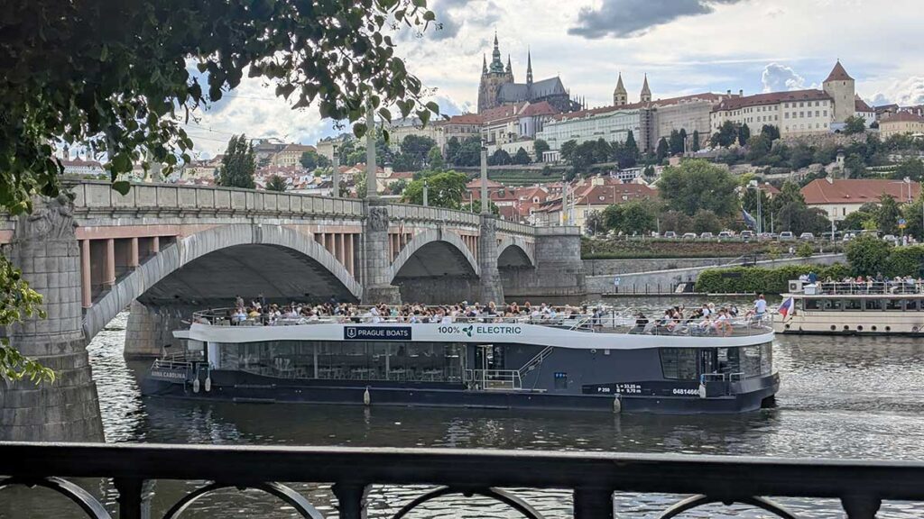 Barco turístico navegando por el río Moldava frente al Puente de Carlos en Praga durante el atardecer.